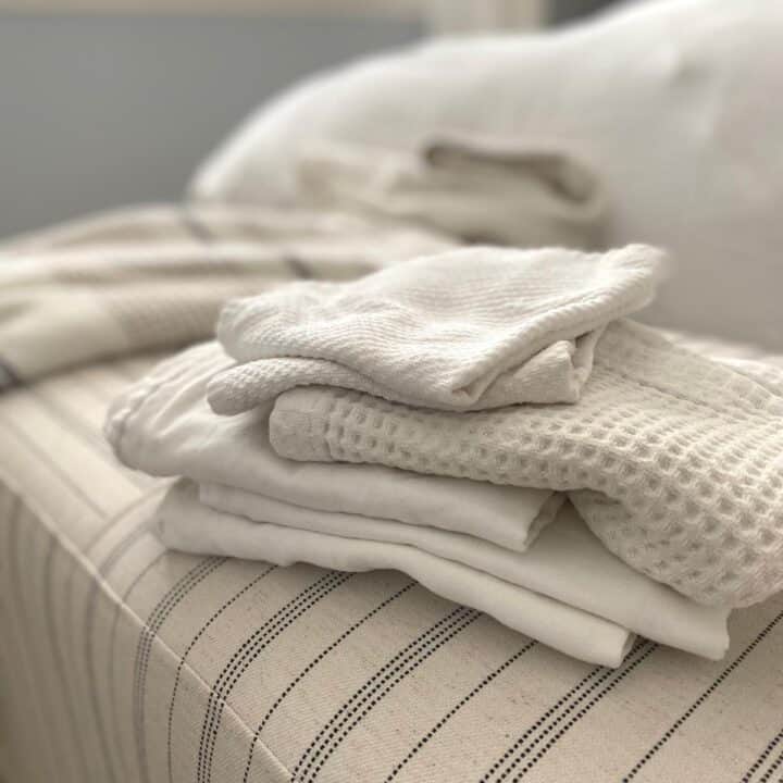 Stack of various textures of white cotton cleaning cloths on top of a striped ottoman