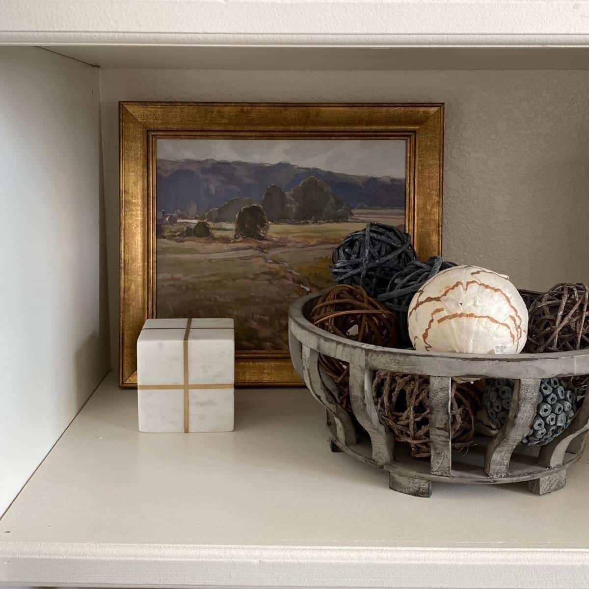 Landscape artwork styled behind marble block and basket with fillers.