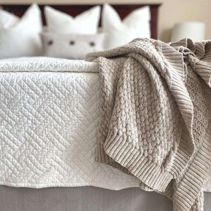 White diamond pattern organic cotton coverlet on bed, with cable knit blanket draped on top