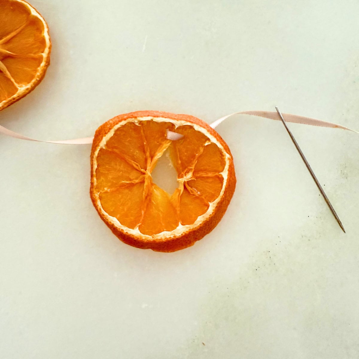 process threading ribbon through orange slice for garland