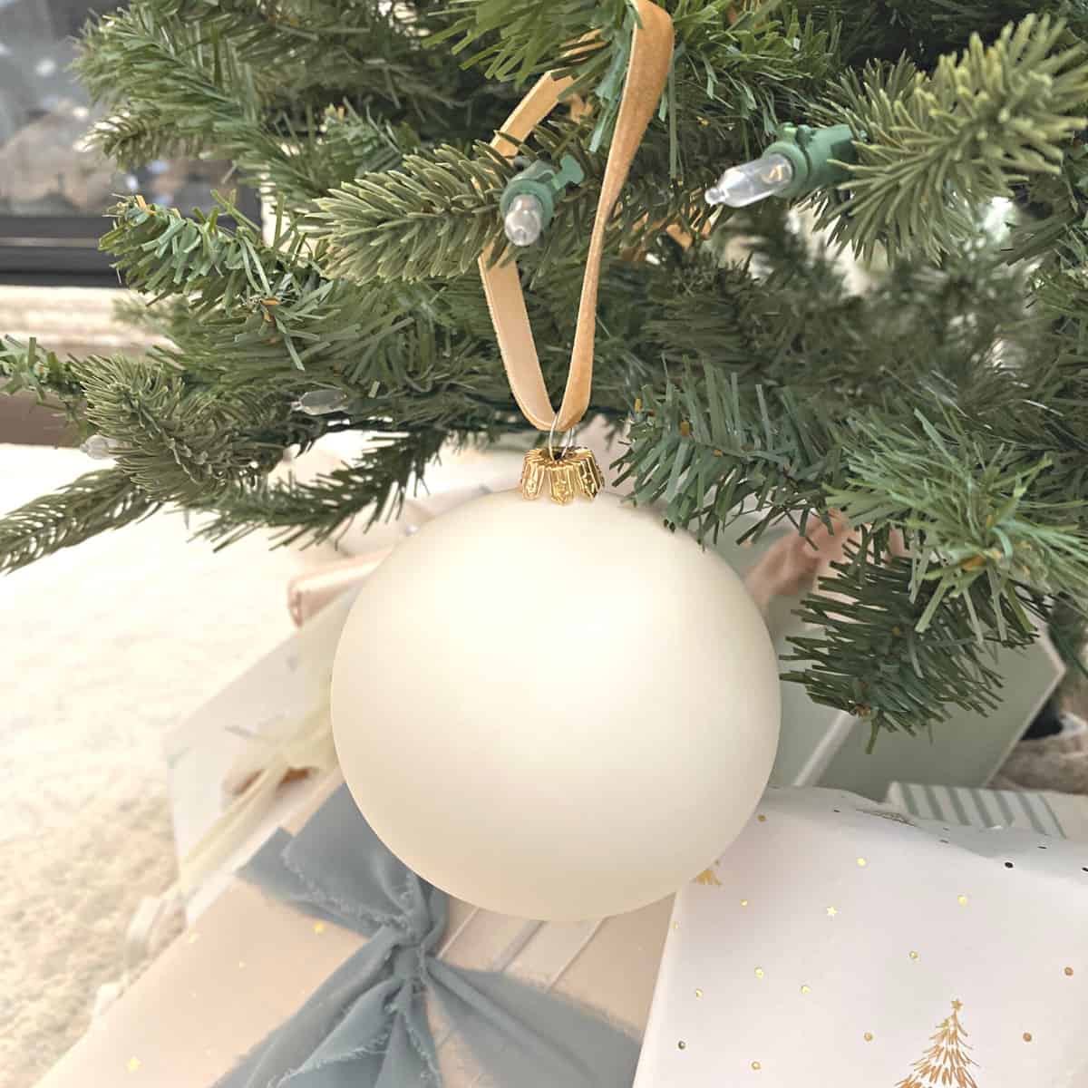 Matte white glass ball ornament adorns the Christmas tree, hanging above presents