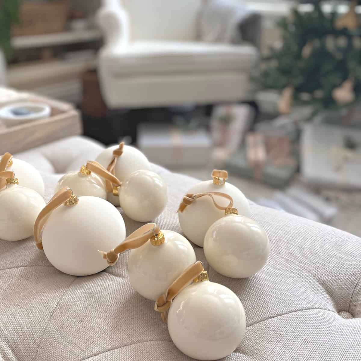 Matte and glossy white glass ball ornaments atop a tufted ecru linen ottoman