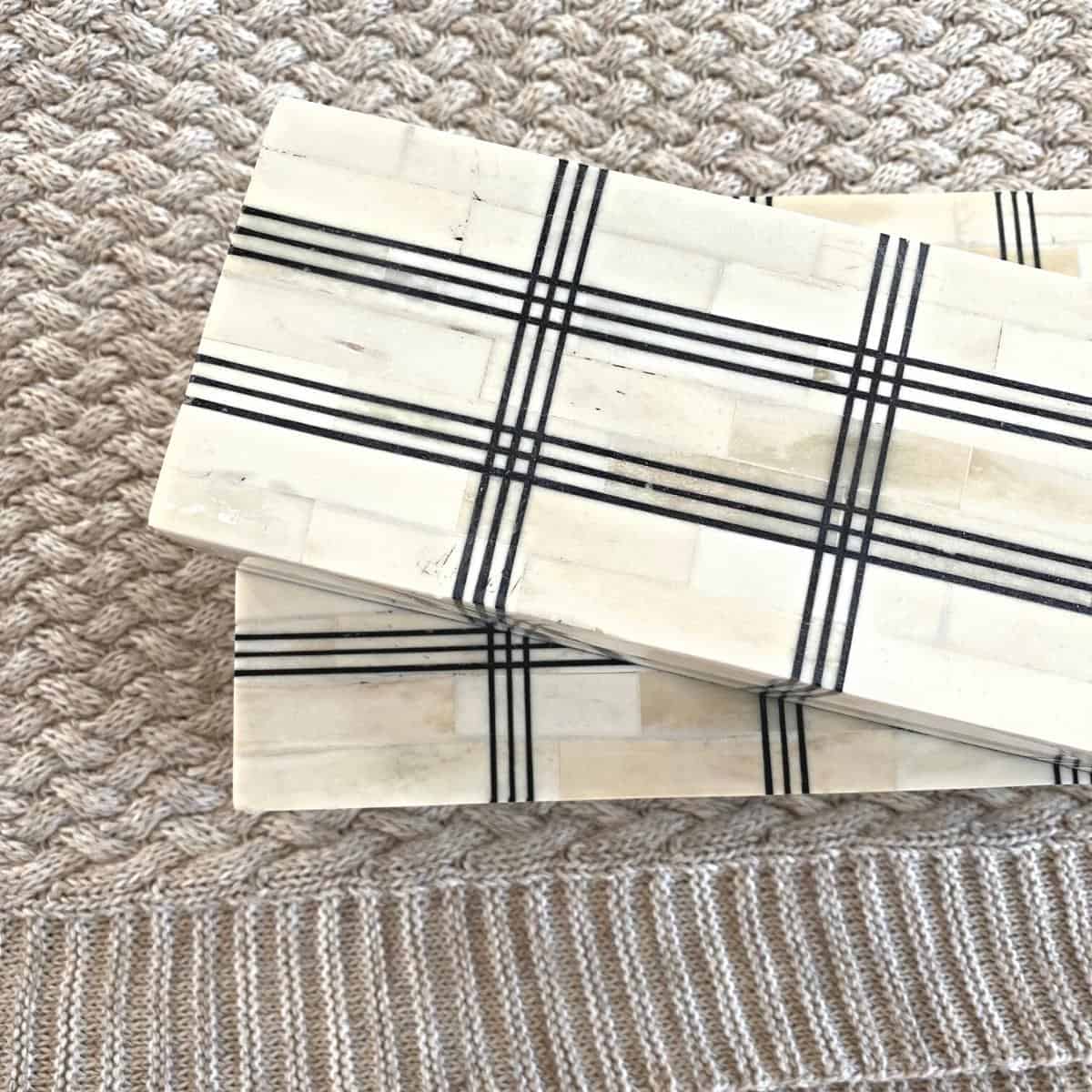 Wide grid bone boxes on top of a beige bed blanket from above