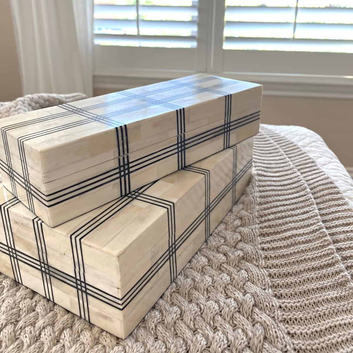 Wide grid bone boxes on top of a beige bed blanket