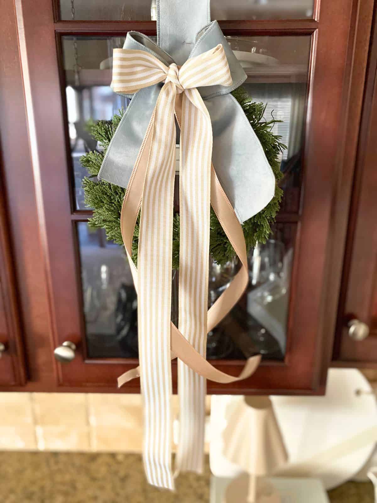 wreath decorated with taupe and blue ribbon hanging on glass cabinet door