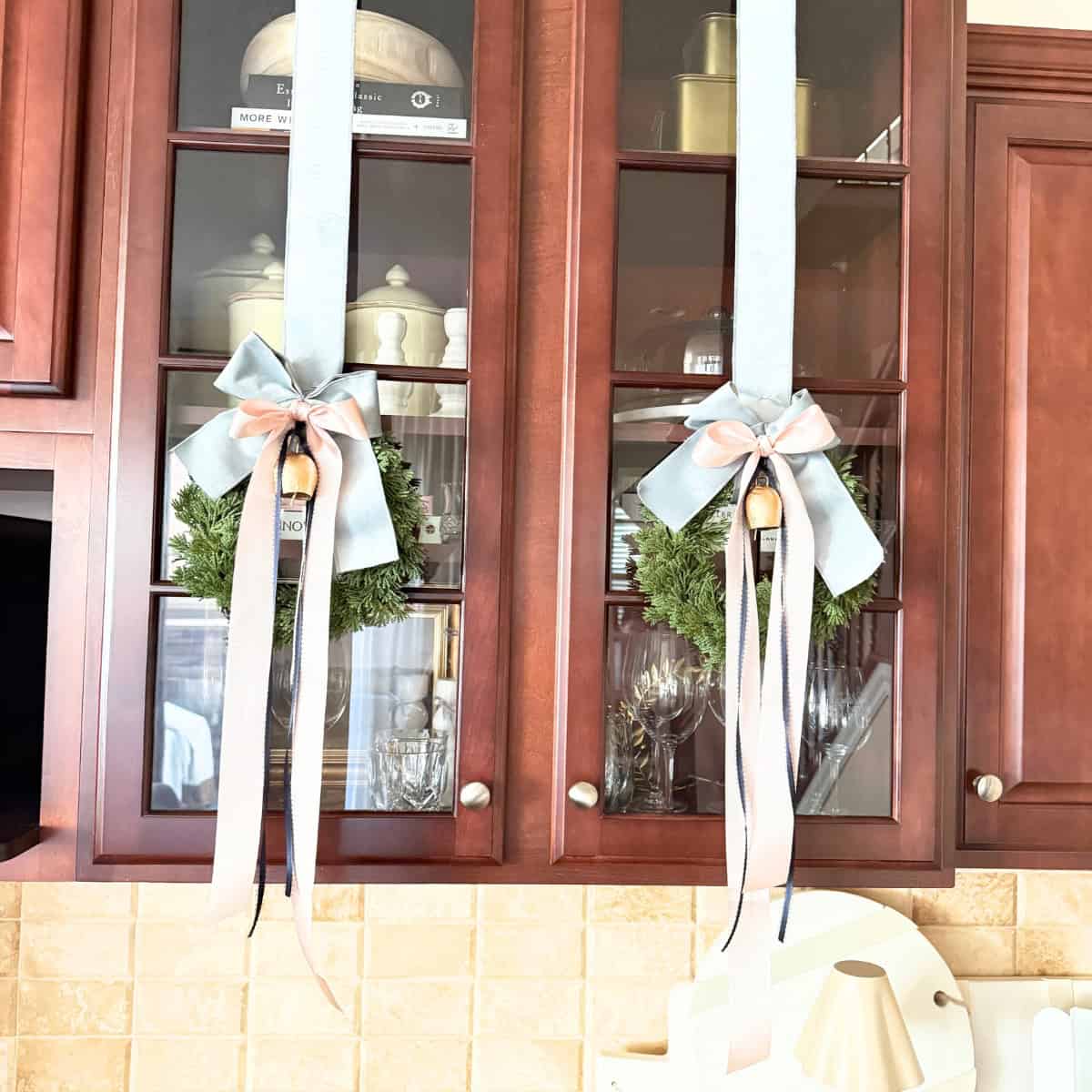 mini wreaths hanging from cabinet with ribbons and a bell