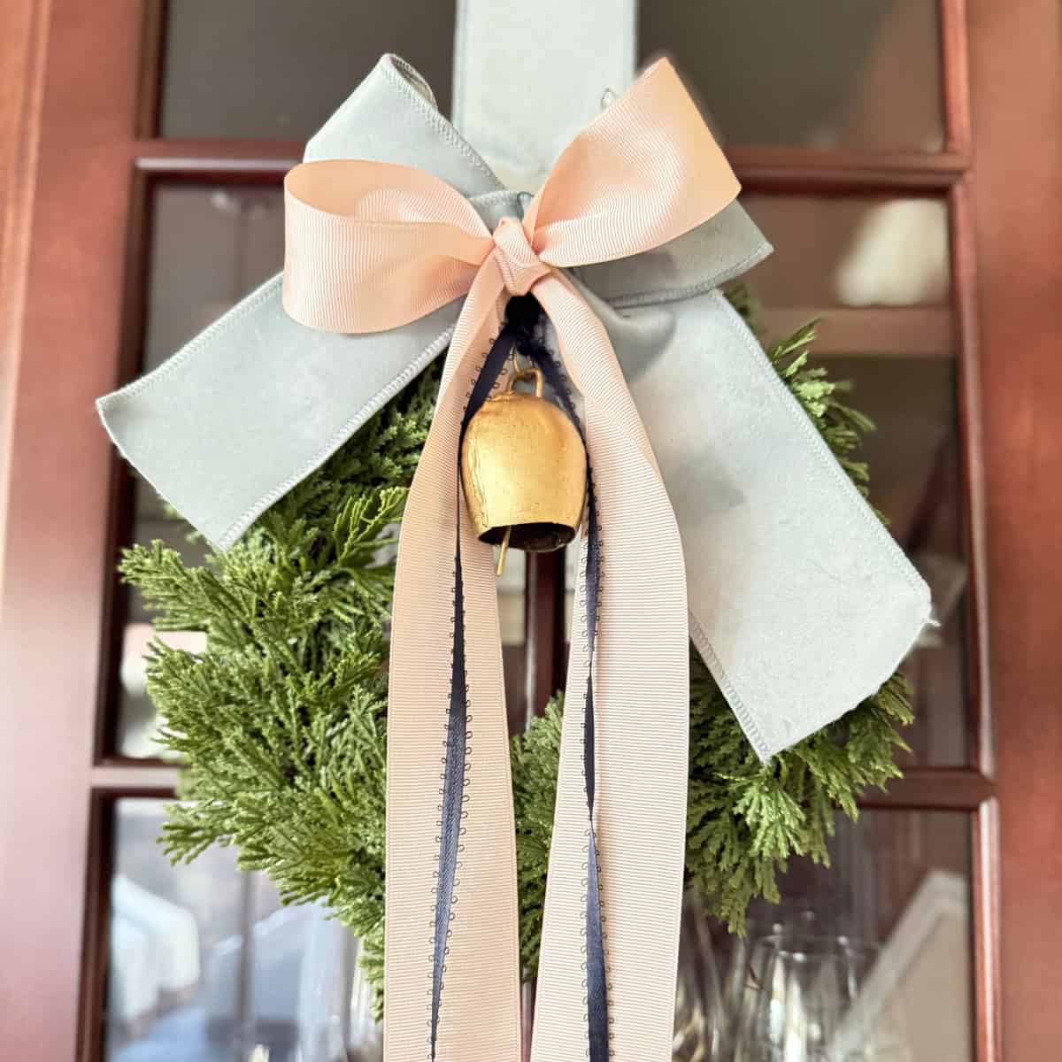 mini wreath hanging from cabinet with ribbons and a bell